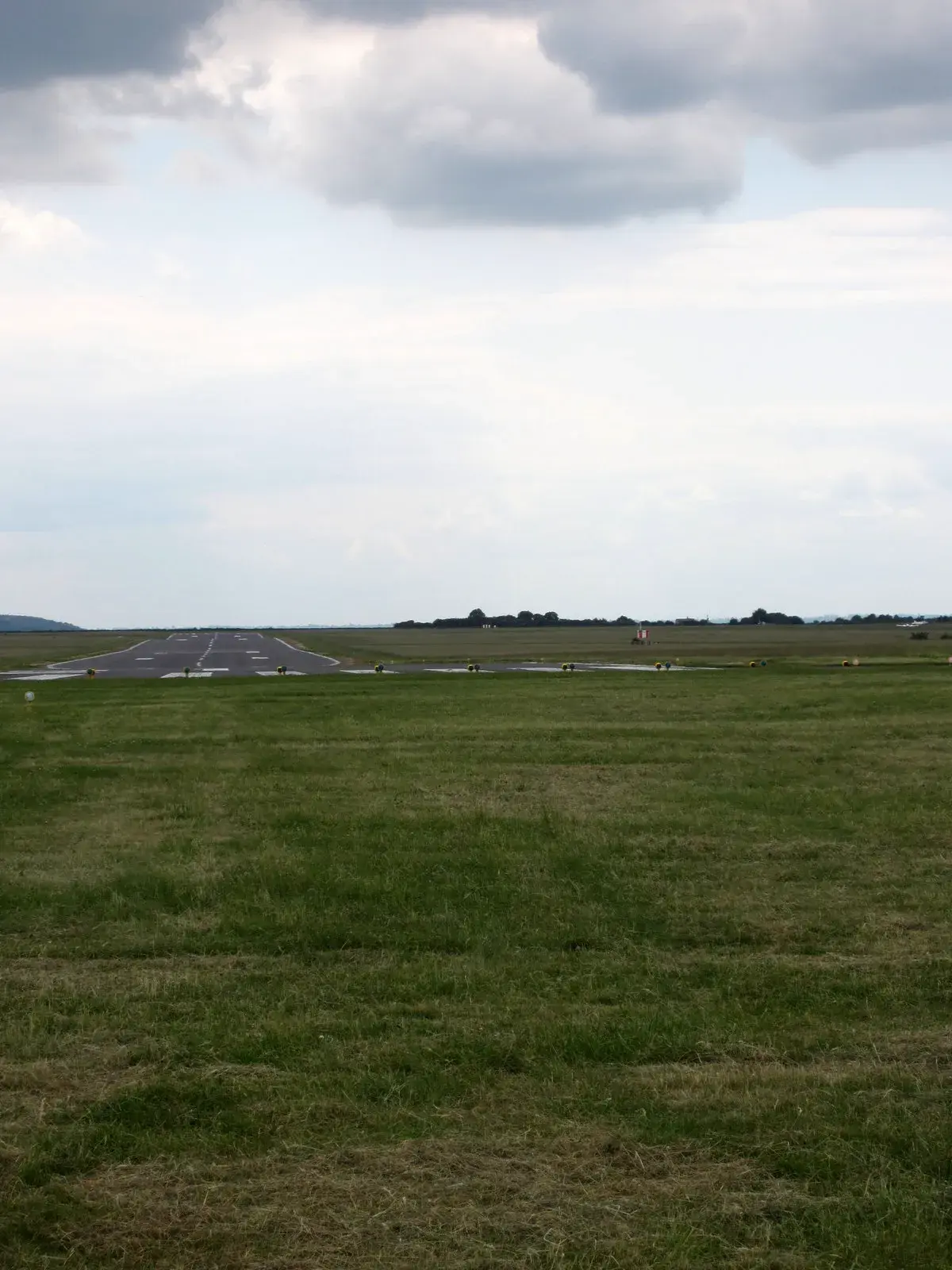 A runway surrounded by grassy fields under a cloudy sky